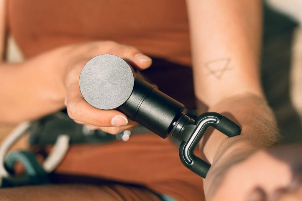 woman using compact massage gun on forearm